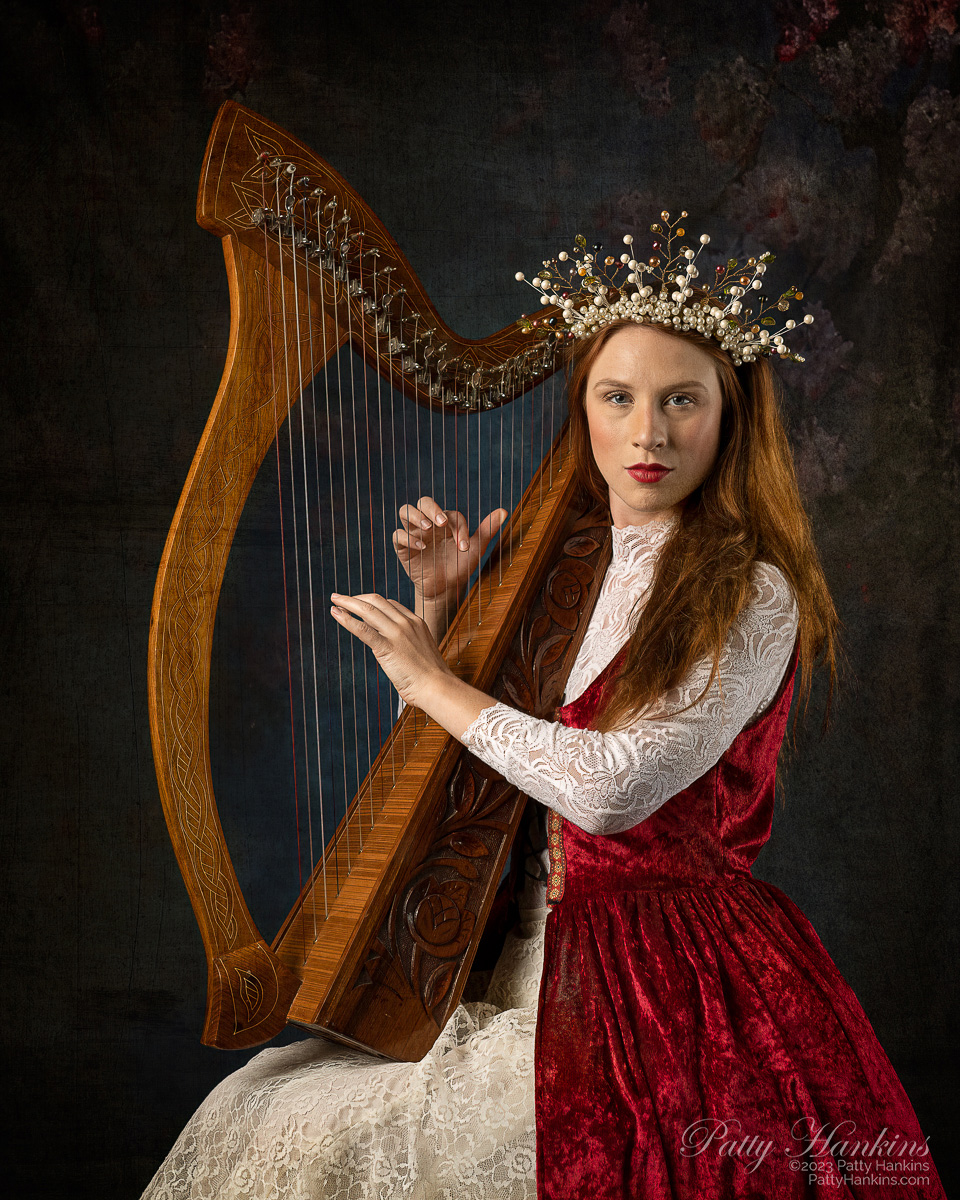 Astrid Kallsen wearing a renaissance inspired red over dress - over a white lace dress, wearing a pearl headpiece - playing her harp